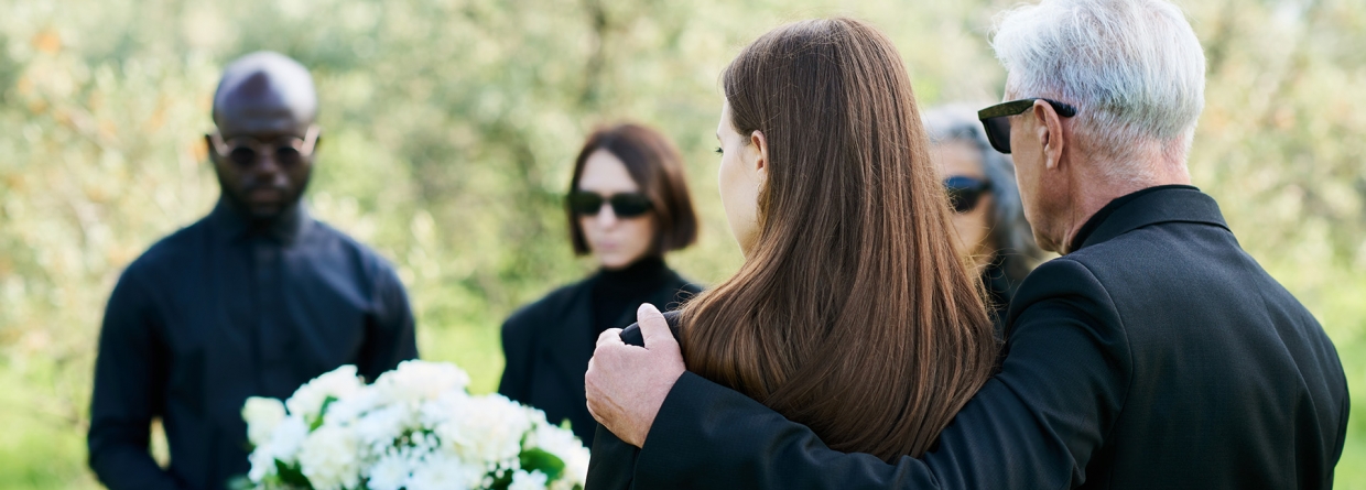 Uitvaart; mensen staan om een kist met bloemen